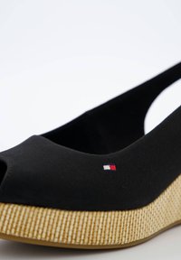 Zwarte stoffen wedge-schoen met open teen, een gestructureerde zool van natuurlijke vezels en een klein geborduurd logo in rood, wit en blauw.