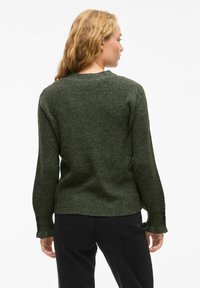 Groene gebreide trui met een gestructureerde afwerking, met lange mouwen en een ronde halslijn. De zoom heeft een licht uitgerafeld randje.