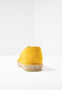 Chaussure espadrille en daim jaune avec un talon bas, présentant une semelle en jute tissée et une texture lisse. Pas de motifs visibles ni de détails en matériel.