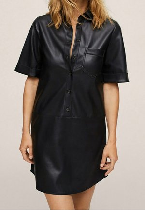 Schwarzes kurzärmeliges Hemdkleid aus Kunstleder mit Knöpfen vorne und Brusttasche, getragen von einer Person mit blonden Haaren.