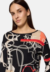 Czarna bluzka z długim rękawem z kremowymi, czerwonymi i pomarańczowymi abstrakcyjnymi wzorami, z szerokim dekoltem i luźnym krojem. Wykonana z miękkiego materiału.