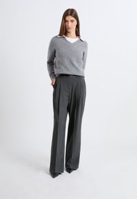 Szary wełniany sweter z dekoltem w kształcie litery V i jasnoróżowym kołnierzykiem, zestawiony z szarymi spodniami z wysokim stanem i karczkiem oraz czarnymi butami w szpic.