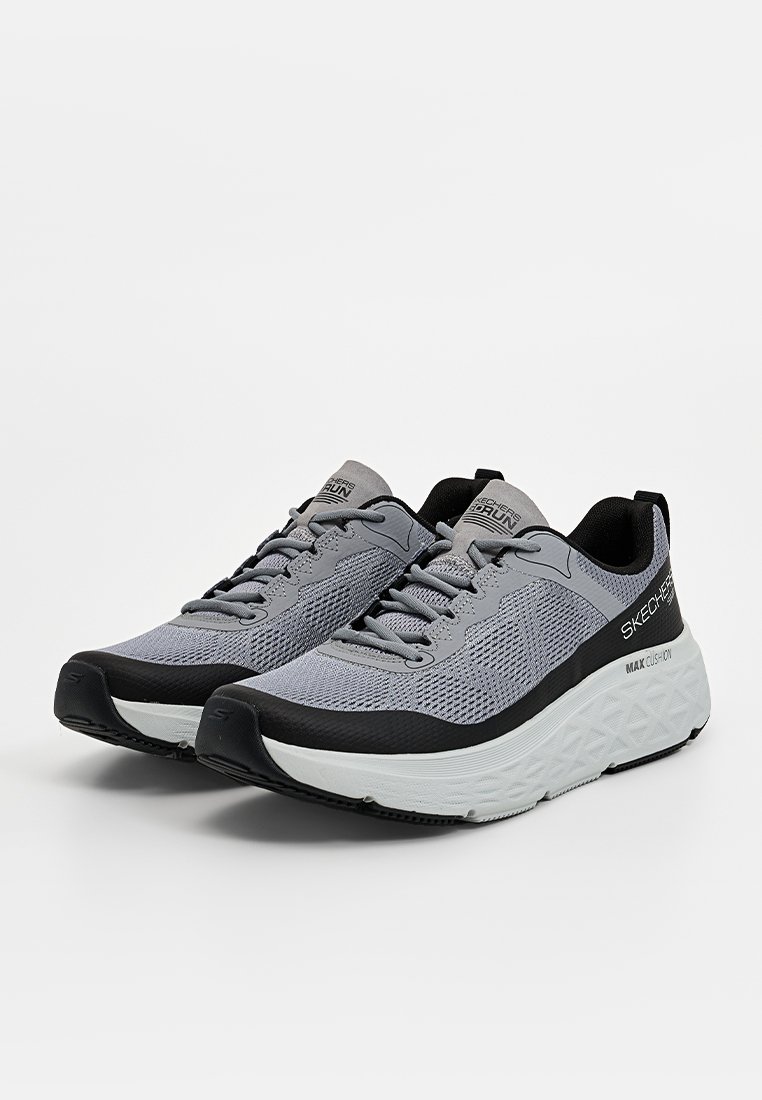 Zapatillas deportivas grises con acentos negros. Parte superior de malla, diseño de cordones, suela blanca gruesa con patrón texturizado. Marca visible en el lateral.