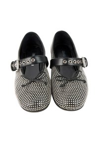 Paire de chaussures style Mary Jane noires avec des clous argentés, des nœuds noirs sur les orteils et des brides réglables à boucle sur le dessus.