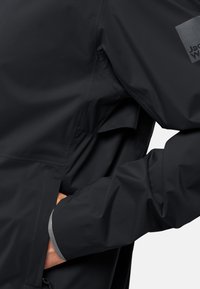 Giacca impermeabile nera con una texture liscia, dotata di una tasca con zip e rifiniture riflettenti sui polsini, e un logo sulla manica.