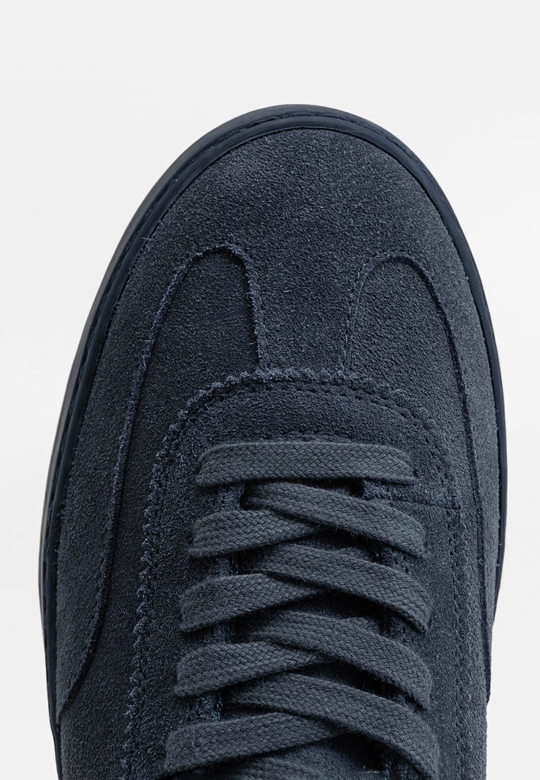 Donkerblauwe nubuck sneaker met een ronde neus, platte veters en een gestructureerd oppervlak, met nadruk op stiksels langs de zijkanten en de neuskap.