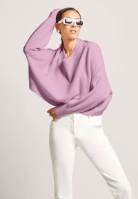 Licht paarse oversized trui met brede mouwen, gecombineerd met witte aansluitende broek. De stof lijkt zacht en ademend te zijn.