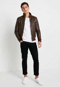 Pruunist nahast pommijakk ribatakiste ja kaelusega, valge T-särgi kohal, mustade pükstega ja valgete sportkingadega.