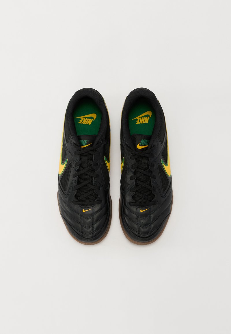 Zapatillas deportivas negras con parte superior de cuero texturizado, acentos amarillos y plantillas verdes. Presenta un diseño de cordones y suelas de goma.
