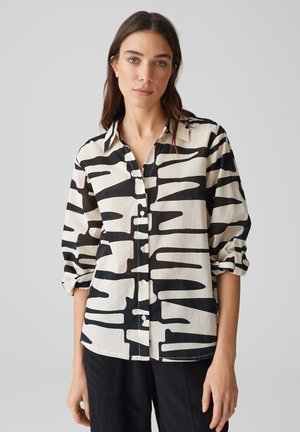 Chemise à motif noir et blanc avec un devant à boutons, un col évasé et des manches retroussées, fabriquée en tissu léger.