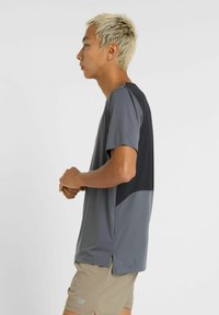 Grå atletisk skjorte med korte ærmer, med et sort paneldesign på den øverste del af ryggen, kombineret med beige shorts.