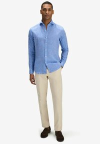 Ljusblå linnedskjorta med knäppbar krage, slim fit, långa ärmar och en enfärgad textur, kombinerad med beiga byxor och mörka skor.