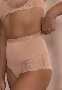 Beige höga trosor i mjukt tyg, med en spetskant längs botten och en mjuk, satinliknande midja.