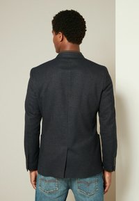 Donkerblauwe blazer met een gladde textuur, enkele rugsplit en notch-lapels, gecombineerd met lichtblauwe denim jeans.