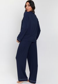 Conjunto de loungewear azul marino hecho de tejido suave, que incluye una camiseta de manga larga con un bolsillo y pantalones anchos con ribetes blancos en los dobladillos.