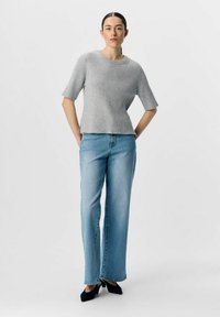 Top grigio a coste con maniche corte, abbinato a jeans a gamba larga blu chiaro e décolleté nere a punta.