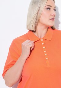 Oranžové polo tričko z bavlny s límečkem a sedmi knoflíky, krátkými rukávy a hladkým povrchem.