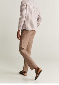 Camisa de manga larga a rayas en rosa claro y blanco, combinada con pantalones de lino beige y sandalias marrones con diseño de tiras.