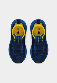 Μπλε και ναυτικό αθλητικό παπούτσι με κίτρινες λεπτομέρειες, με επάνω μέρος από δίχτυ, στρογγυλή μύτη και δέσιμο με κορδόνια. Διαθέτει γλώσσα με λογότυπο και υφή στην σόλα.
