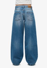 Jeans de denim azul de pierna ancha con un acabado desgastado, que cuentan con una cintura alta, grandes bolsillos traseros y dobladillos elásticos. Material de algodón duradero.