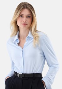 Hellblau gestreiftes Hemd mit Knöpfen aus glattem Stoff, mit klassischem Kragen und einer einzelnen Brusttasche, kombiniert mit einem schwarzen Gürtel.