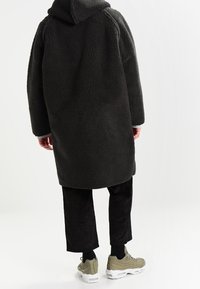 Tummanharmaa fleecetakki hupulla, väljä malli ja resorit hihansuissa. Yhdistetty mustiin corduroy-housuihin ja vaaleanvihreisiin lenkkareihin.