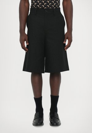 Black Bermuda shorts with a straight cut, featuring a button closure, flat front, and side pockets. Worn with black loafers and socks.