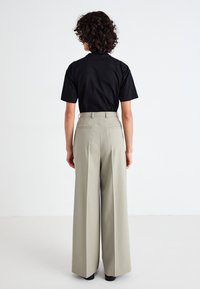 Hoge taille, wijde broek in licht olijfgroen met een gladde textuur, achterzakken en riemlussen. Gecombineerd met een getailleerd zwart t-shirt.