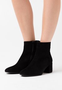 Botas de tobillo de ante negro con punta afilada, cierre con cremallera lateral y tacón grueso. Textura suave sin patrones visibles.