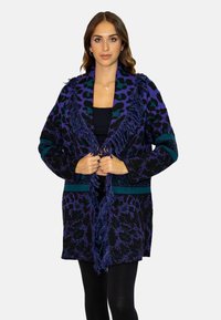 Cardigan nero con stampa leopardata viola e teal, bordo in frange lungo il colletto e bordatura geometrica. Maniche lunghe e design aperto davanti.