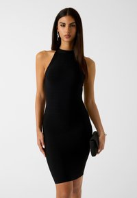 Abito nero aderente con collo alla halter e texture a costine, design fino al ginocchio, accompagnato da una piccola pochette nera testurizzata.