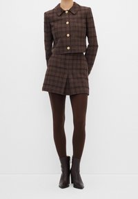 Brun ternet croppet jakke med guldknapper, kombineret med en matchende brun mininederdel og mørkebrune strømpebukser, fuldendt med høje hæle støvler.