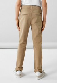 Chinos beige con una vestibilità dritta, dotati di due tasche posteriori, una texture liscia e indossati con sneakers bianche.
