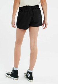 Shorts en coton noir avec une taille élastique, dotés d'une poche arrière et d'une coupe décontractée, associés à des baskets montantes noires.