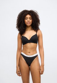 Μαύρο σουτιέν με λείες θήκες και ρυθμιζόμενους ιμάντες, σετ με μαύρο στρινγκ με λευκή μέση που φέρει το λογότυπο «TOMMY HILFIGER».