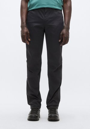 Fekete, egyenes szabású nadrág könnyű anyagból. Övhurkokkal és oldalzsebekkel rendelkezik, fekete, texturált lábbelivel párosítva.