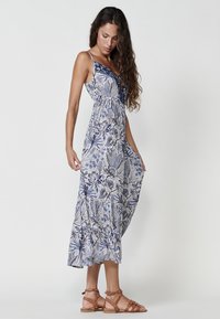 Rochie maxi florală în nuanțe de albastru și alb, cu bretele subțiri, talie plisată și margine în straturi. Pur și simplu cu sandale bej cu curea.