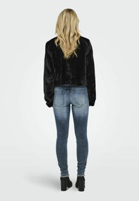 Felpa nera e pelosa, tagliata corta, abbinata a jeans skinny blu scoloriti e stivali alla caviglia con tacco blocco neri. La vista posteriore mette in evidenza la texture e la vestibilità.