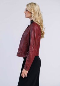 Veste en cuir rouge au design ajusté, avec une fermeture éclair à l'avant et deux poches latérales, présentée de côté. Texture lisse avec des détails de couture minimaux.