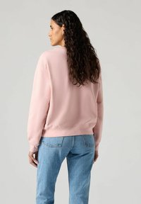 Light pink sweatshirt with a relaxed fit, ribbed cuffs, and hem; paired with blue denim jeans, displaying soft fabric texture.