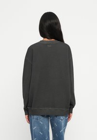 Σκούρο γκρι φούτερ με ραμμένο λαιμό και μανίκια, με χαλαρή γραμμή και λεπτομέρειες ραφής στο στρίφωμα.