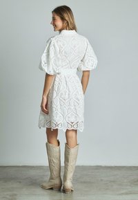 Biała koronkowa sukienka z bufkami, z wyciętymi wzorami i falbaniastym dołem. W połączeniu z beżowymi kowbojkami ozdobionymi haftem.