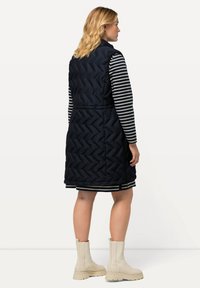 Marineblau gesteppte Weste mit Fischgrätmuster, kombiniert mit einem gestreiften Langarmshirt und cremefarbenen Stiefeletten, mit hohem Kragen und seitlichen Reißverschlüssen.