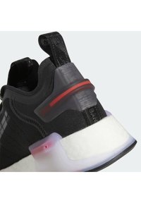 Black athletic shoe featuring a textured knit upper, translucent heel clip with a red accent, and a white cushioned sole.