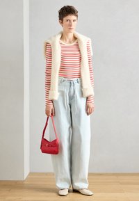 Ριγέ κόκκινο και άσπρο μακρυμάνικο μπλούζα, κρεμ ψεύτικο γούνινο γιλέκο, ανοιχτό μπλε παντελόνι φάρδυ, κόκκινη τσάντα, ουδέτερα φλατ παπούτσια, μίνιμαλ περιβάλλον.