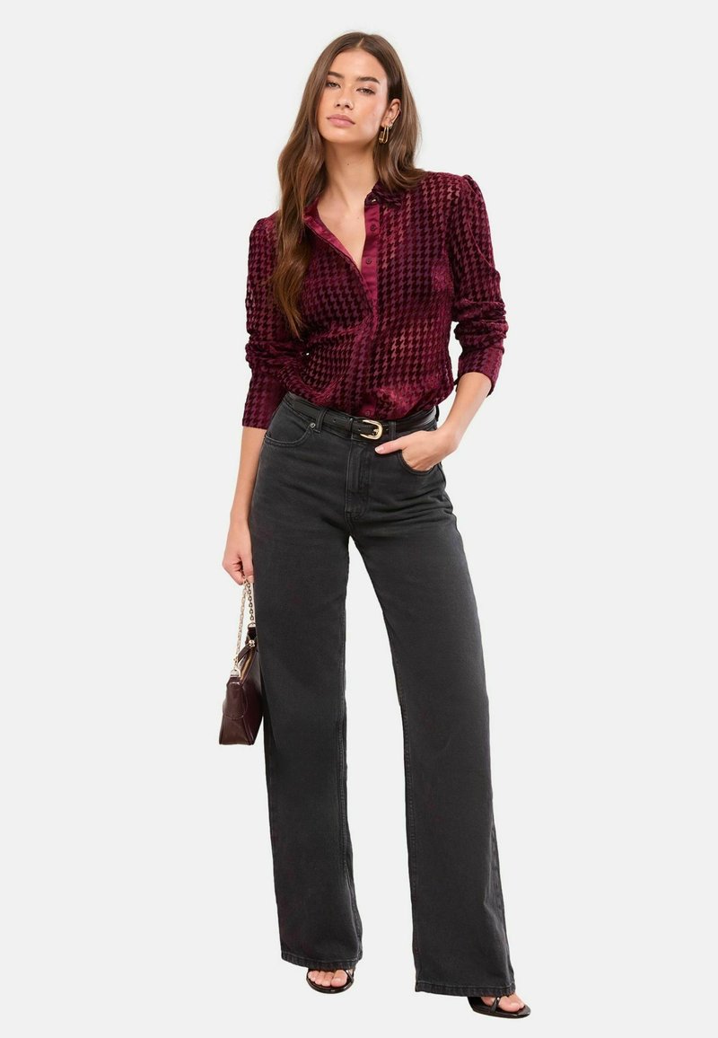 Burgundijas krāsas rakstaina samta krekls ar garām piedurknēm, kombinēts ar augsto vidukli melnajām platmalu biksēm. Aksesuāros iekļauta maza soma.