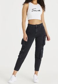 Pantalones cargo negros con múltiples bolsillos laterales, cintura alta y pierna ajustada. Combinados con un top corto sin mangas blanco con letras negras.