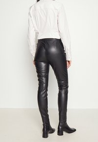 Svarta läderleggings med slim fit, hög midja, slät yta och detalj med bakre söm, tillsammans med en vit skjorta.