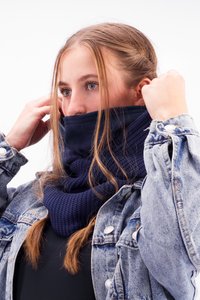 Navy blue knitted neck warmer with textured pattern, worn under a denim jacket. The fabric appears soft and cozy, covering the lower face.
