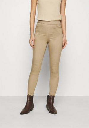Pantalons skinny beiges avec une texture lisse et une taille haute, assortis à des bottines en cuir marron présentant un motif crocodile.